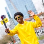 Black content creator wearing a yellow hoodie shooting a video on his phone