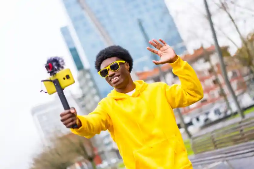 Black content creator wearing a yellow hoodie shooting a video on his phone