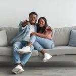Black couple watching TV on a grey couch