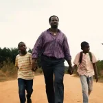 Still from the film, My Fathers Shadow. Folarin walking hand in hand with his two sons.